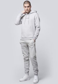 Light gray hoodie with drawstrings and kangaroo pocket, paired with matching joggers. Both have a soft texture and logo accent. White sneakers.