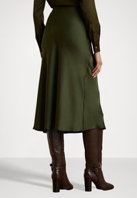 Grønn satin skirt med utvidet søm og en sideslitt. Kombinert med brune lærstøvletter til kneet og en tettsittende bluse.