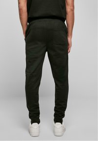 Pantalons de survêtement noirs en matériaux doux, avec une coupe ajustée, une taille élastique et une poche arrière. Associés à des baskets blanches.