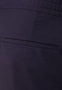 Tmavě modrá látka s texturovaným povrchem, obsahující jednu zadní kapsu. Kapsa má horizontální otvor a čistý, přizpůsobený design.