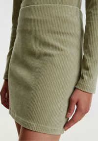 Jupe courte en velours côtelé couleur kaki avec une texture à côtes verticales, coupe ajustée et manches longues avec poignet ajusté.