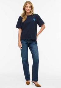 Tmavě modré bavlněné tričko s krátkými rukávy a světle modrým srdíčkem na hrudi, kombinované s tmavými džínami a hnědými lodičkami na podpatku.