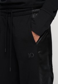 Zwarte joggingbroek met een verstelbare tailleband, met een gladde textuur en een klein geborduurd "10" op de zijkant van de zak.