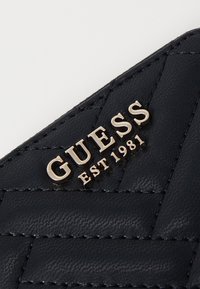 Portefeuille matelassé bleu marine en matériau synthétique avec le logo doré "GUESS EST 1981". Surface(texturée avec un motif en diamant.