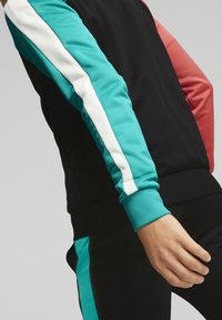 Svart atletisk jacka med teal, vit och korallfärgade accenter. Har en färgblockerad design på ärmar och manschetter, med en slät yta.