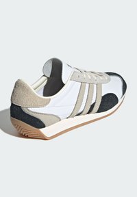 Sneaker bianco con accenti in suede grigi e neri. Presenta tre strisce grigie, un collare imbottito e una suola in gomma testurizzata.