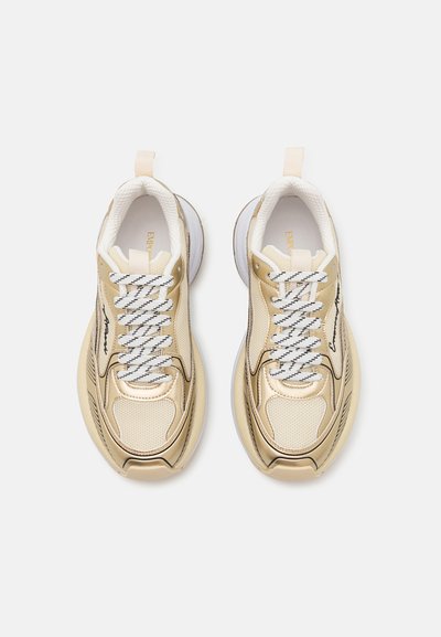 Ljusguld sneakers med vita detaljer, strukturerad mesh och syntetiskt material, med tjocka vita snören och en kraftig sula design.