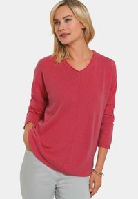 V-Ausschnitt Pullover in leuchtendem Pink, mit lockerem Sitz, überschnittenen Schultern und gerippten Bündchen. Weiche Strickstruktur.