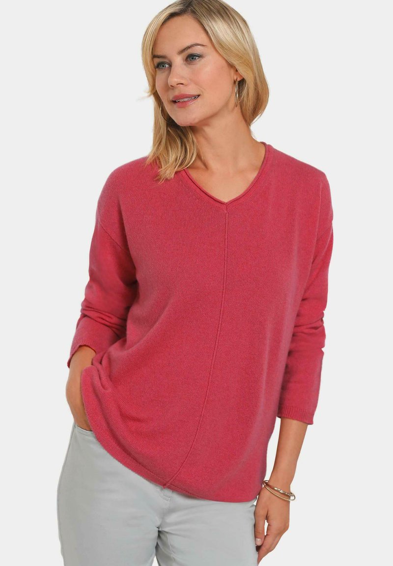 V-Ausschnitt Pullover in leuchtendem Pink, mit lockerem Sitz, überschnittenen Schultern und gerippten Bündchen. Weiche Strickstruktur.