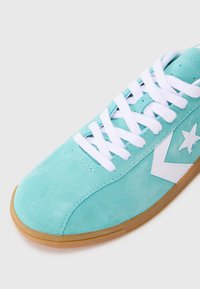 Suedesneakers i lys turkis med hvide snørebånd, udstyret med et hvidt stjernelogo og gummisål. Glat tekstur med rund toe.