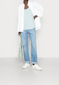 Witte button-up shirt, lichtblauw tanktop, lichtgewassen rechtliggende jeans, witte sneakers en een lichtgroene handtas met een textuurafwerking.