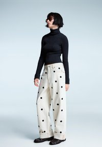 Črna rebrasta turtleneck, bele široke hlače z črnimi pikami in črna obutev. Obleko dopolnjujejo sončna očala.