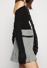Zwarte geribbelde off-shoulder trui met lange mouwen, gecombineerd met een blauw-witte houndstooth flared rok. Bevat een zwarte gevlochten tasriem.