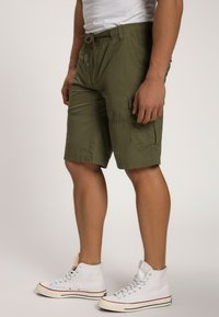 Olivengrønne cargoshorts med elastisk talje, snøre, flere lommer og en afslappet pasform. Båret med hvide højtop sneakers.
