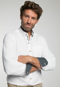 Witte overhemden met een staande kraag, voorzien van gestreepte donkere manchetten en contrasterende afwerking. Voorzak en zilveren knopen.