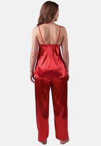 Rotes Satin-Camisole und Pyjama-Set mit dünnen verstellbaren Trägern. Die weit geschnittenen Hosen haben eine glatte Textur und ein fließendes Design.