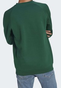 Grön sweatshirt med rund halsringning, raglanärmar, en slät yta och ribbad nederkant, bärs med ljusblå jeans.