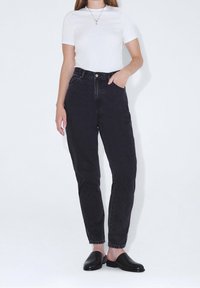 Hög midja svarta denimjeans med rak ben, med fem fickor och knäppning med knappar. Kombinerat med en figurnära vit t-shirt och svarta träskor.