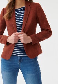 Blazer texturé couleur rouille à coupe ajustée, associé à un haut à rayures bleu marine et blanc et un jean en denim bleu.