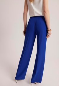 Spodnie z wysokim stanem i szerokimi nogawkami w intensywnym niebieskim kolorze, charakteryzujące się gładką fakturą i zwiewnym krojem, w zestawieniu z prostą białą bluzką.
