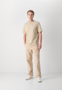 Beige bavlněné tričko s krátkým rukávem, spárované s světlobéžovými kalhotami a bílými teniskami s hnědým logem. Minimalistický design a střih.