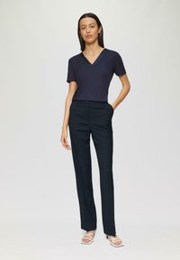 T-shirt marine à col en V, pantalons foncés ajustés avec un motif subtil, et talons blancs à lanières. Tissu doux, design ajusté et silhouette structurée.
