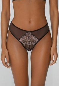 Zwarte netten slipjes met intrikate lila kant ontwerpen in een diamantvorm, met een klein strikdetail in het midden en contrasterende bies.