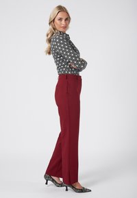 Czarna i biała bluzka w wzory, czerwone spodnie i czarne szpilki w wzory. Bluzka ma długie rękawy; spodnie mają prosty krój.