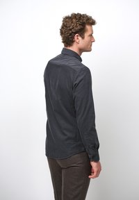 Camicia grigia scura con colletto, dotata di maniche lunghe e una superficie liscia. La vista posteriore mostra una vestibilità su misura e un design semplice.