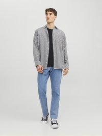 Schwarz-weiß kariertes Hemd über einem schwarzen T-Shirt, kombiniert mit hellblauen Jeans und schwarzen Sneakers. Einfaches, lässiges Design.