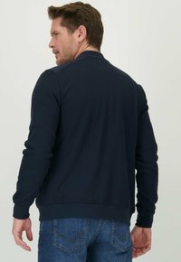 Marineblauwe sweatshirt met lange mouwen, ribgebreide manchetten en zoom, een gladde textuur en een ronde halslijn, gedragen over blauwe jeans.