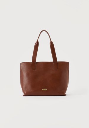 Geantă tote din piele maro cu două curele și o placă mică de metal cu logo, pe un fundal simplu și deschis la culoare.