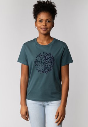 T-shirt en coton bleu sarcelle avec un graphisme marine représentant un cerveau et des éléments floraux, portant la phrase "Ne réfléchis pas trop." Manches courtes et col rond.