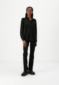 Camisa de veludo preta com riscas verticais, com botões à frente e mangas longas, combinada com calças pretas ajustadas e sapatos pretos robustos.