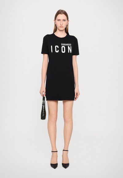Zwart T-shirt jurk van katoen, met een witte "ICON" logo. Gecombineerd met een zwarte tas en zwarte puntige hakken. Eenvoudig, aangesloten ontwerp.