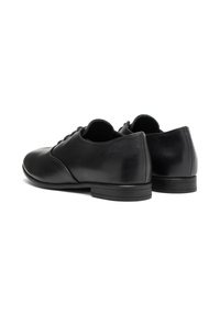 Chaussures en cuir noir avec un profil bas, un bout arrondi et une texture lisse. Elles présentent des lacets et un talon subtil. Design épuré et minimaliste.