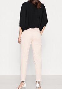 Haut noir surdimensionné à manches courtes, associé à un pantalon fuselé rose clair et des talons blancs à lanières. Tissu lisse avec une coupe décontractée.