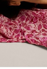 Tela rosa con un patrón floral, que presenta hojas intrincadas y aves. El textil tiene una textura suave, dispuesto sobre una superficie de color neutro.