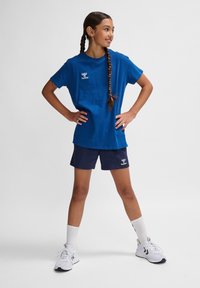 Blå bomullströja med korta ärmar och logotyp, i kombination med navy shorts och vita träningsskor, tillsammans med vita ankelsockor.