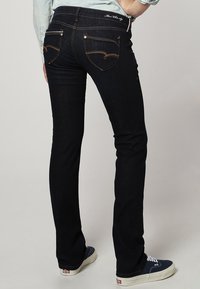 Pantalones vaqueros ajustados en denim oscuro, con bolsillos traseros curvados con detalles de costura, costuras en contraste y una cintura de altura media.