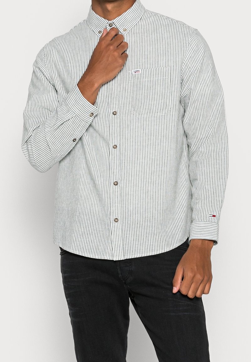 Camisa de botones a rayas verdes y blancas en tejido de algodón, con mangas largas, bolsillo en el pecho y botones plateados. Acentuada con un parche de logo.