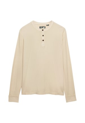 Beżowa koszula henley z długim rękawem, trzema ciemnymi guzikami na listwie i okrągłym dekoltem.