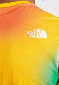 Kurzarm-T-Shirt mit einem Farbverlauf, der von Orange nach Gelb übergeht, und einem weißen Logo auf dem oberen Rücken.