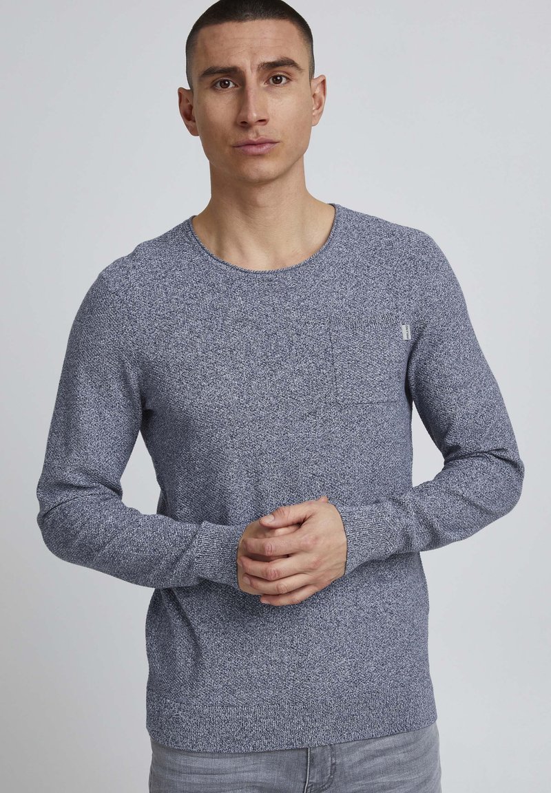 Navy blue knitted pullover with a round neck, long sleeves, and textured pattern. Features a small chest pocket and ribbed cuffs.