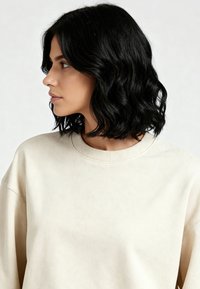 Felpa in cotone beige con scollo rotondo e dettagli a coste. Presenta una vestibilità rilassata e una texture morbida. Modello mostrato di profilo.