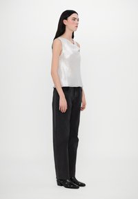 Top sans manches argenté avec un éclat texturé, associé à un jean noir taille haute et des bottines à talons noires avec des accents de perforation.