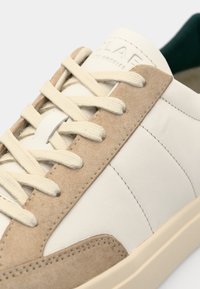 Sneaker in pelle e scamosciato bianco e beige, con lacci piatti, design minimalista e interno verde.