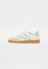 Adidași albi și crem din piele și suede, cu un toc din cauciuc, trei dungi diagonale și detaliu cu logo pe lateral.