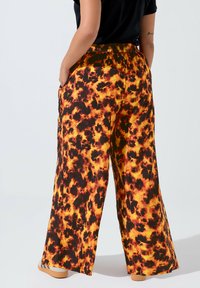 Breda byxor med ett djärvt mönster i svarta, orange och gula lågor. Tyget är lätt, med resårmidja och sidofickor.