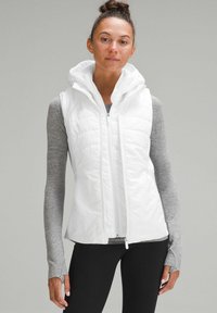 Gilet imbottito bianco con cappuccio e chiusura zip, caratterizzato da un design trapuntato. Indossato sopra una maglietta a maniche lunghe grigia, con tessuto leggero e forma aderente.